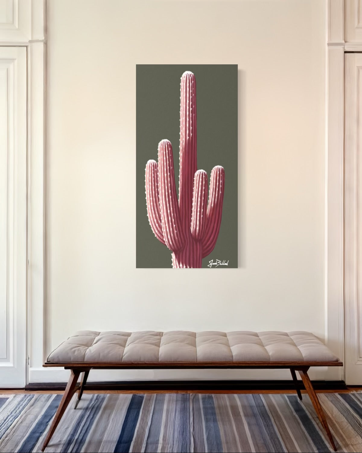 A canvas print featuring a pink saguaro cactus, displayed on a wall above a beige sofa with a wooden frame.
