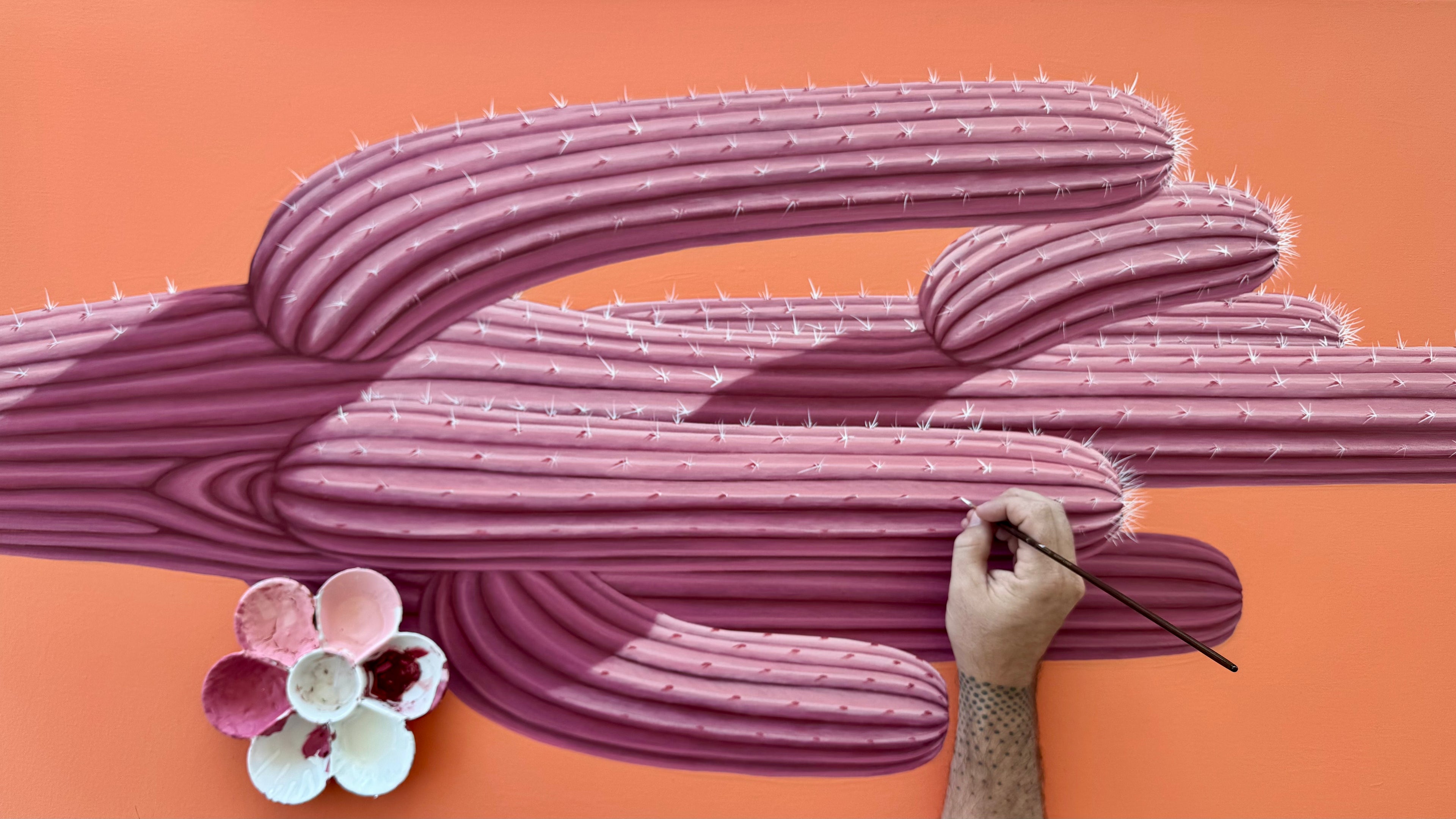 Artistic depiction of a cactus with a hand holding a paintbrush on an orange background